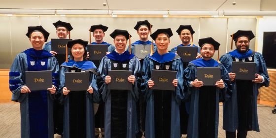 PhD graduates hold their diplomas and look at the camera 